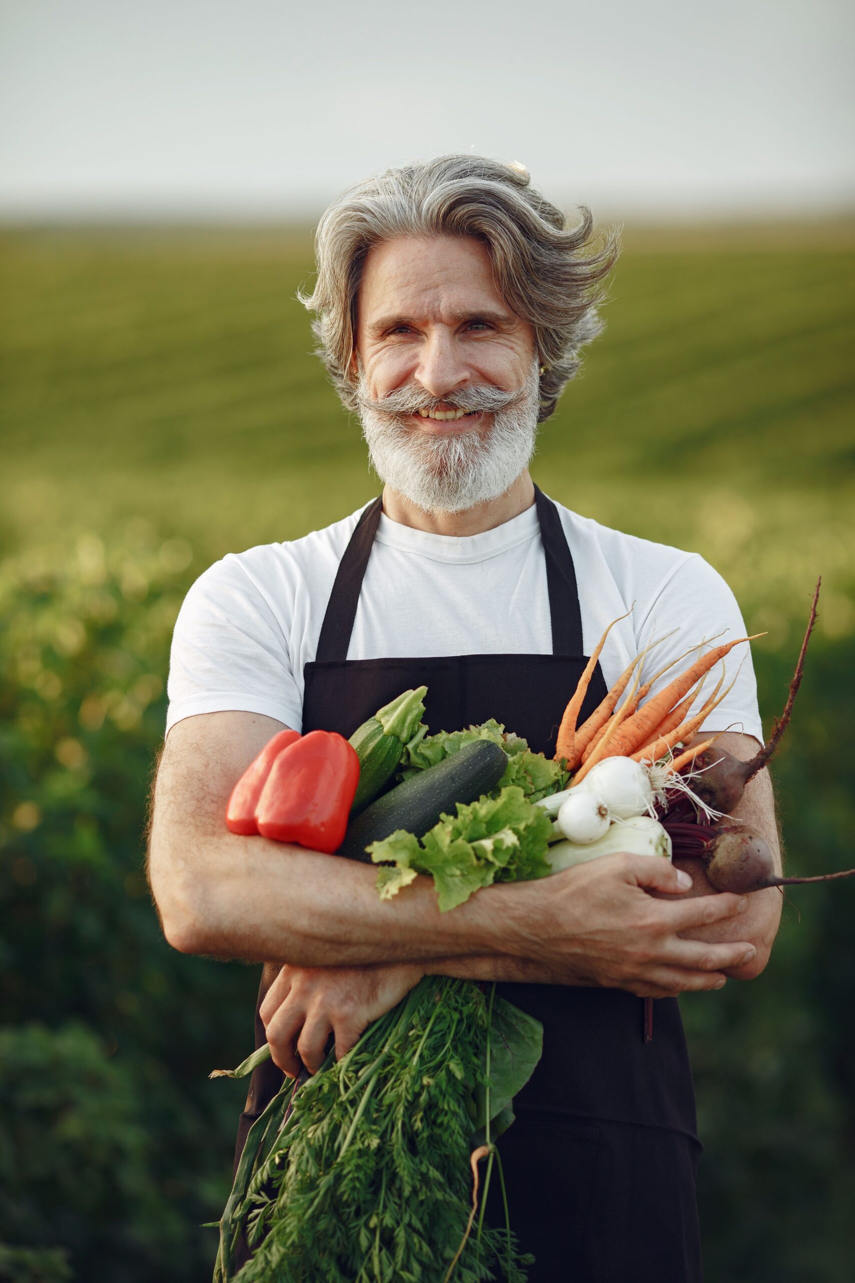 Senior male farmer smiling with fresh vegetables in hand. Outdoor portrait.